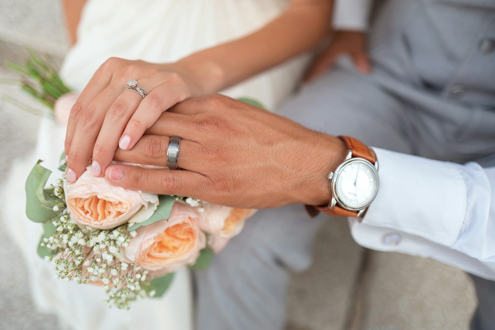 Two hands with wedding rings resting on the bouquet
